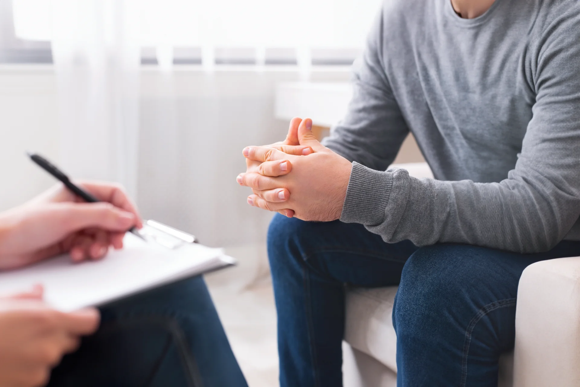 Supportive counseling session with a male patient discussing addiction treatment, therapist taking notes on clipboard, focus on emotional engagement and recovery support.