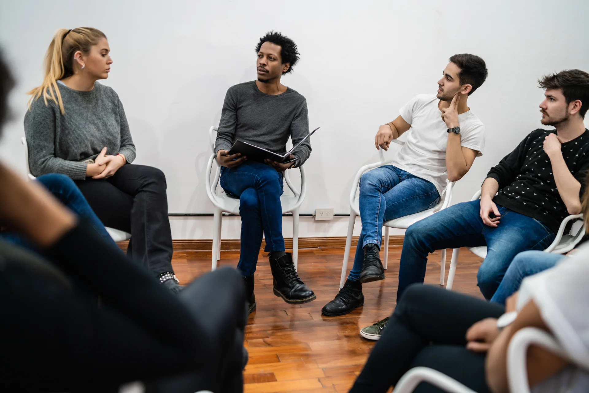 Group therapy session with diverse individuals engaged in discussion, emphasizing support and recovery in addiction treatment context.