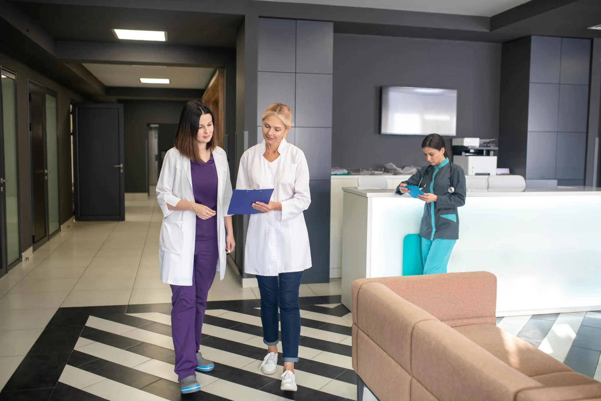 Medical professionals discussing patient care in a modern clinic, with a nurse reviewing a clipboard and another staff member using a tablet, emphasizing teamwork in addiction treatment.