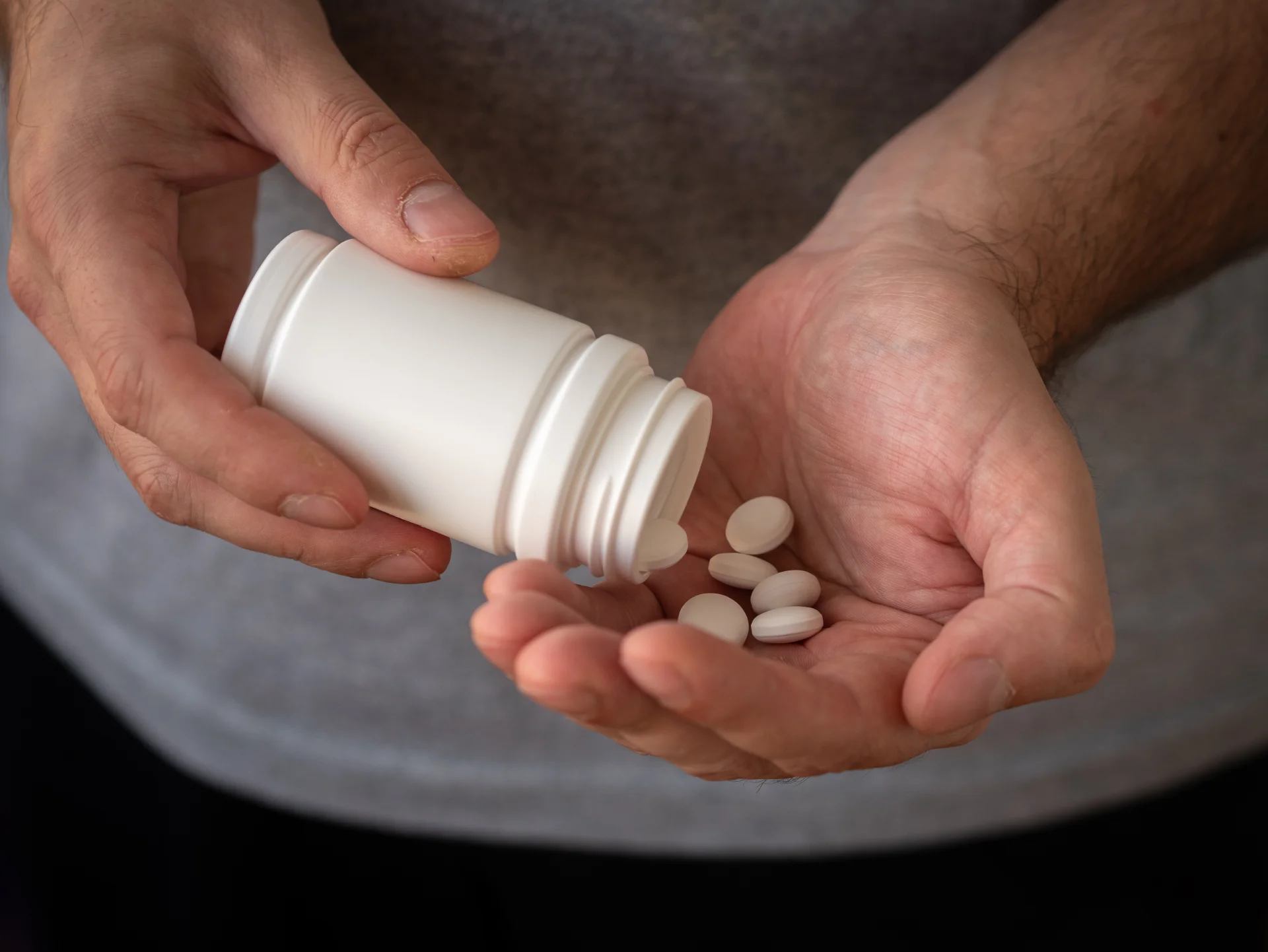 Person holding a white pill bottle and several white pills, illustrating medication management related to Cymbalta (duloxetine) treatment and addiction recovery.