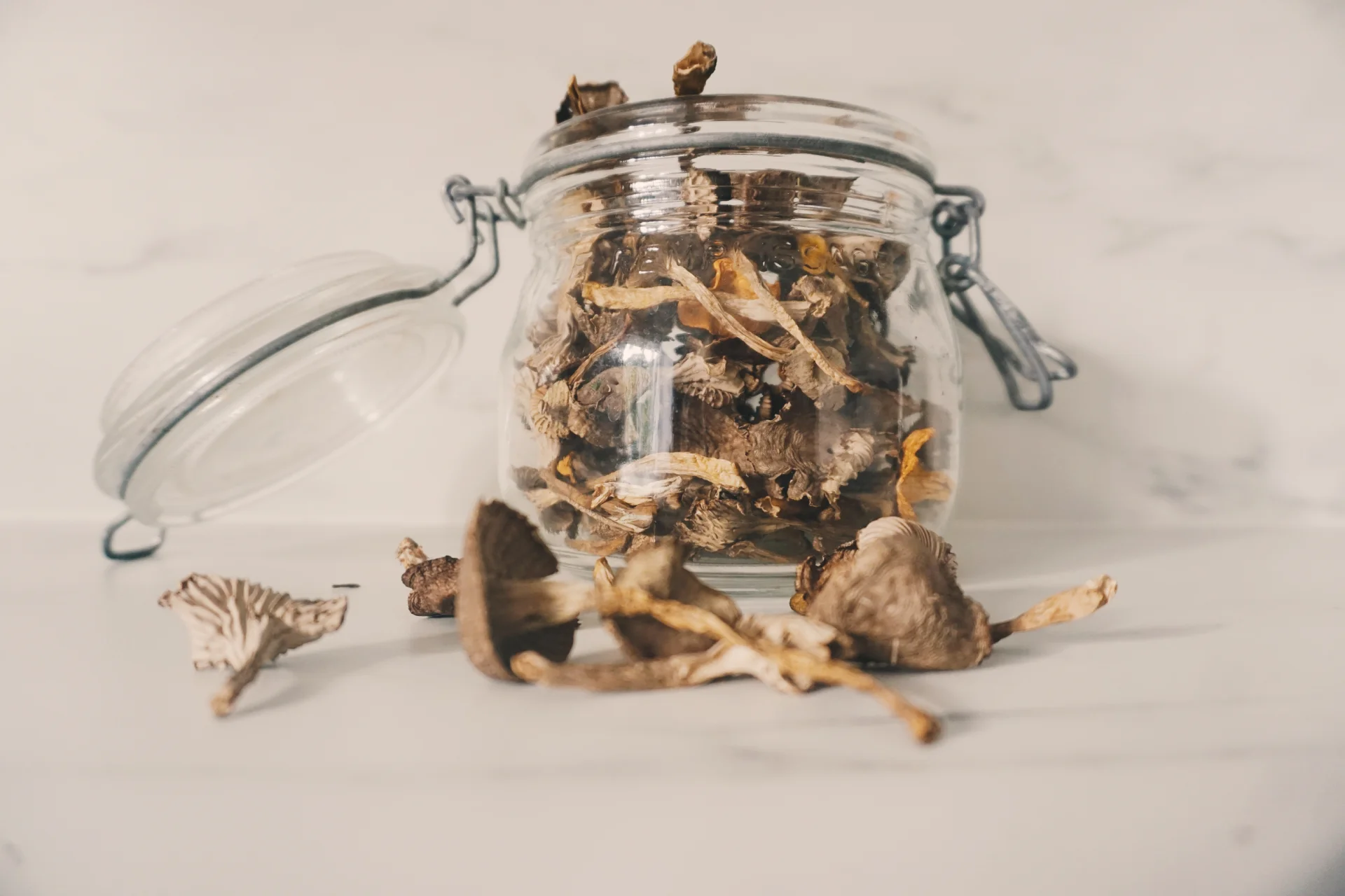 Dried psilocybin mushrooms in a glass jar, with some mushrooms scattered on a surface, representing the context of psilocybin use and addiction treatment resources on Long Island.