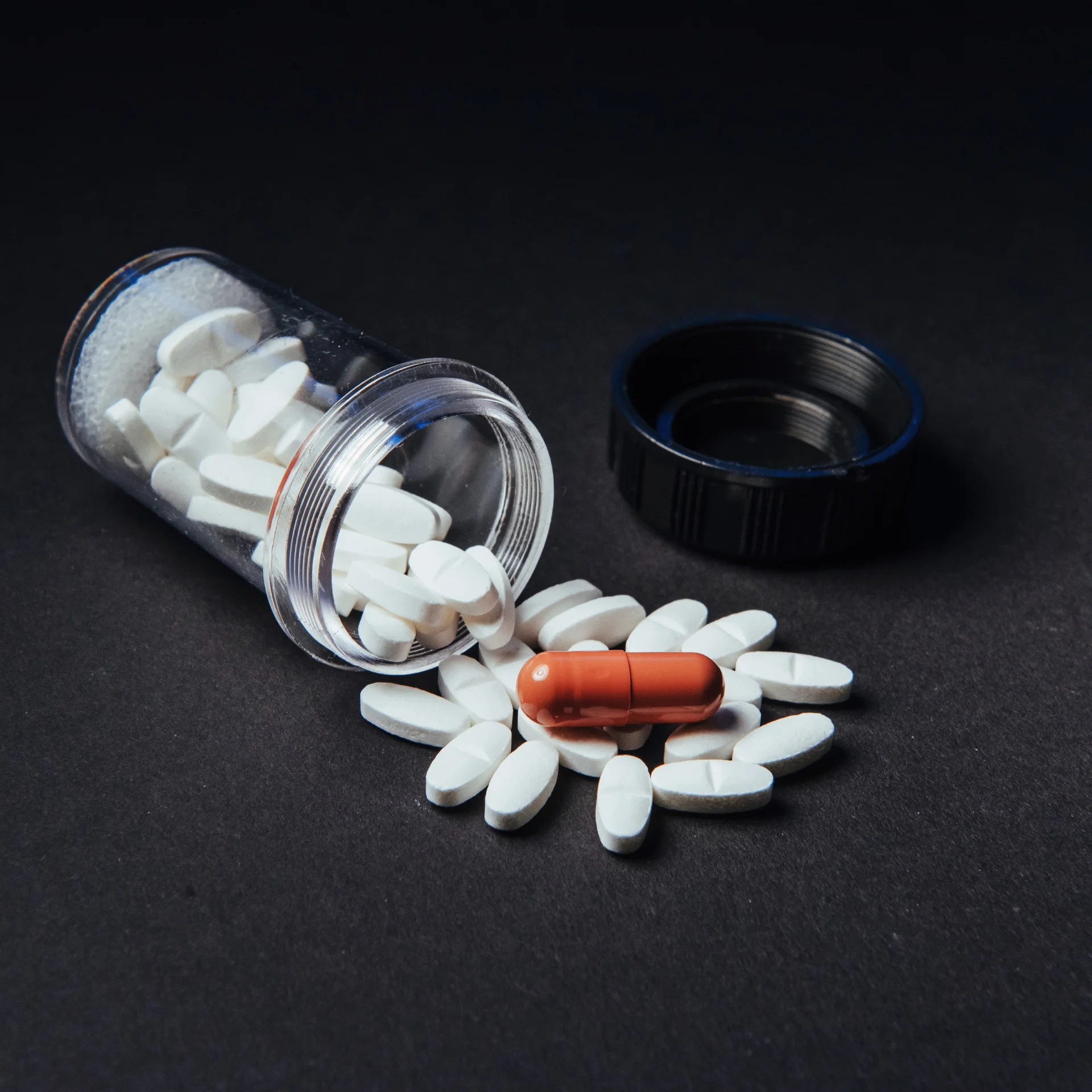 Trazodone pills spilling from a clear prescription bottle alongside a red capsule, representing medication for depression and sleep aid, relevant to addiction treatment resources on Long Island.