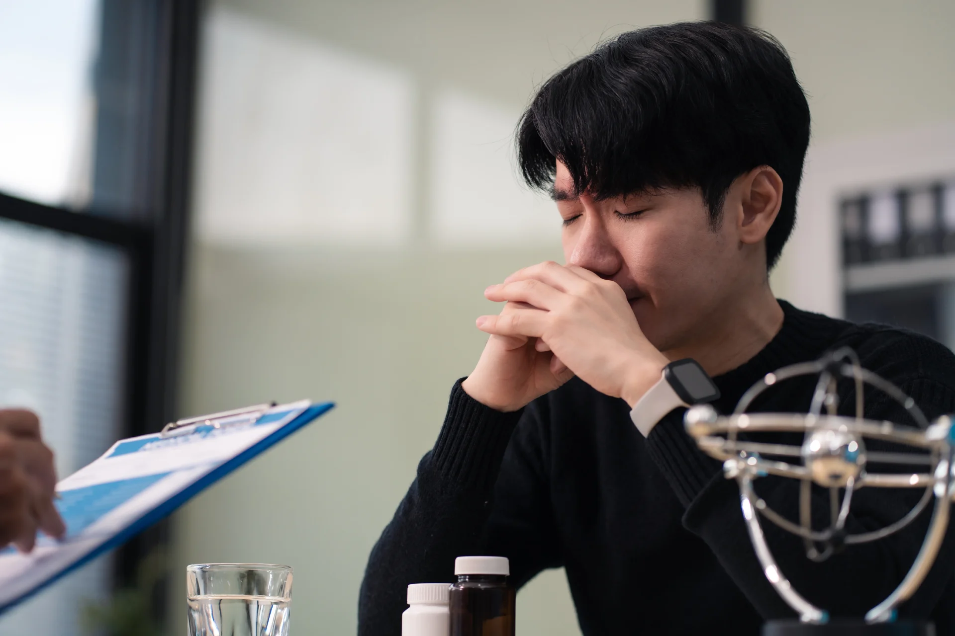 Man sitting at a consultation with a doctor, showing signs of distress, with prescription bottles and a glass of water on the table, emphasizing the emotional impact of addiction treatment discussions.