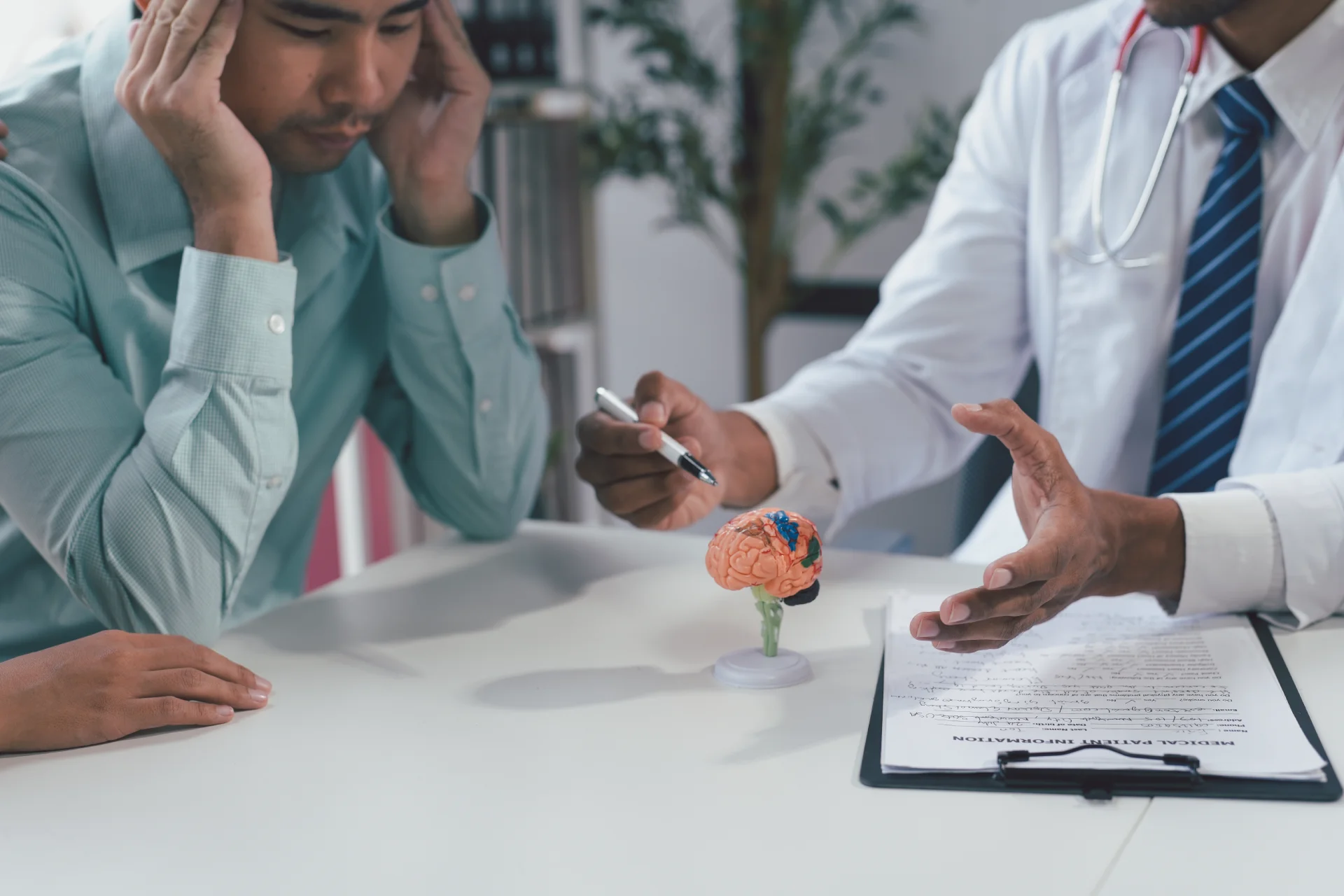 Doctor explaining marijuana's effects on the brain to a patient, with a model brain on the table and a treatment plan document visible.