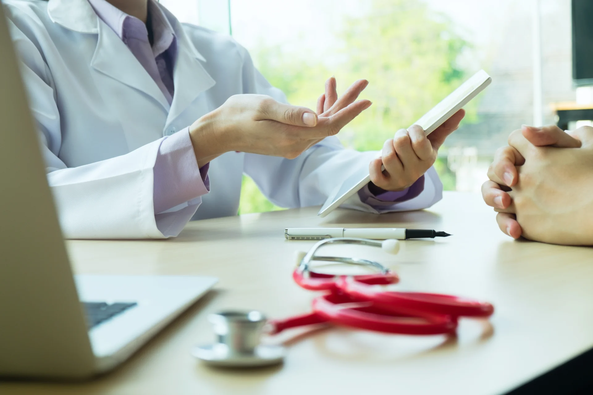Doctor in white coat discussing treatment options with a patient, tablet in hand, stethoscope and laptop on the table, emphasizing personalized care and recovery support for addiction on Long Island.