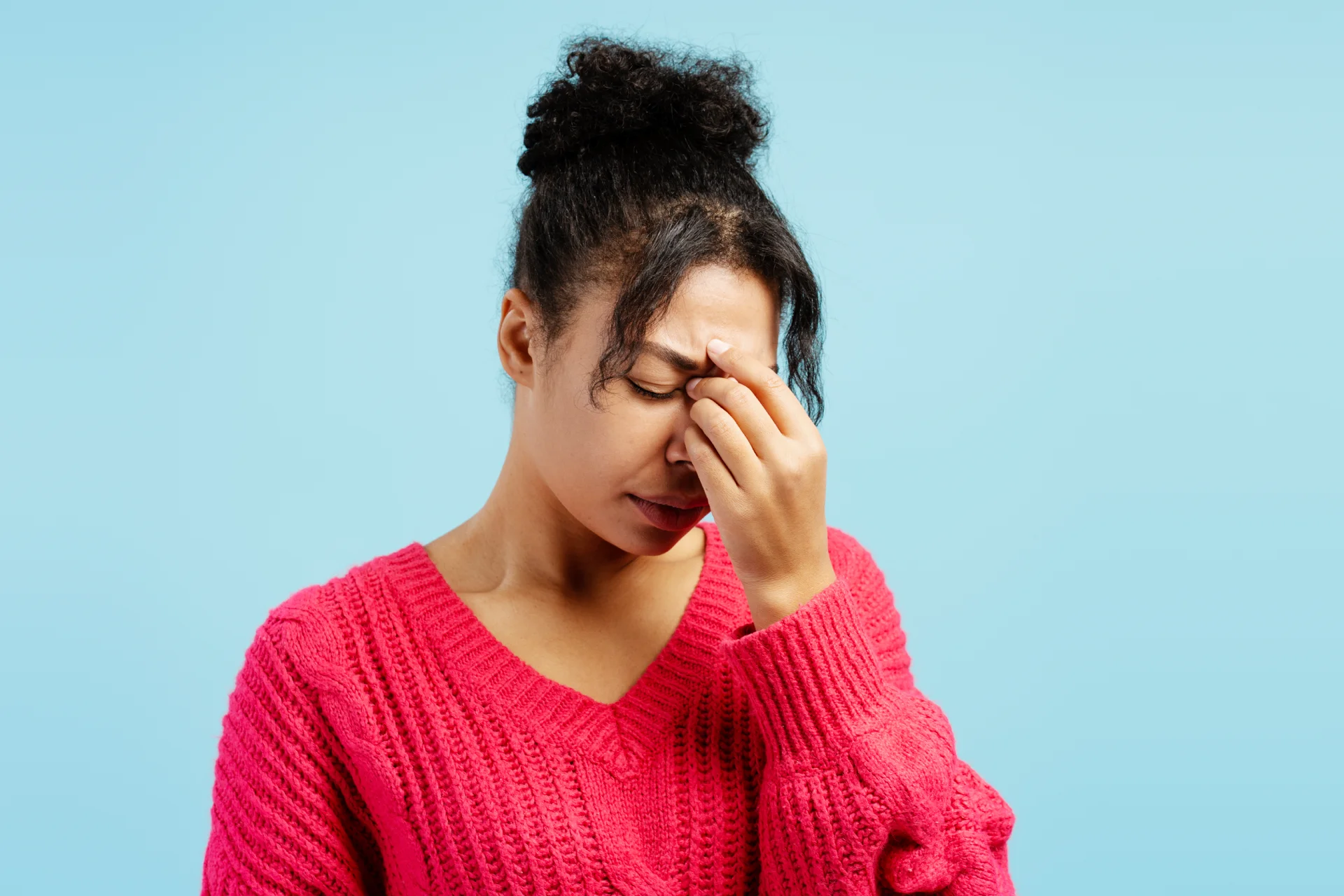 Woman in a pink sweater holding her forehead, expressing discomfort, illustrating common side effect of headache related to bupropion use.