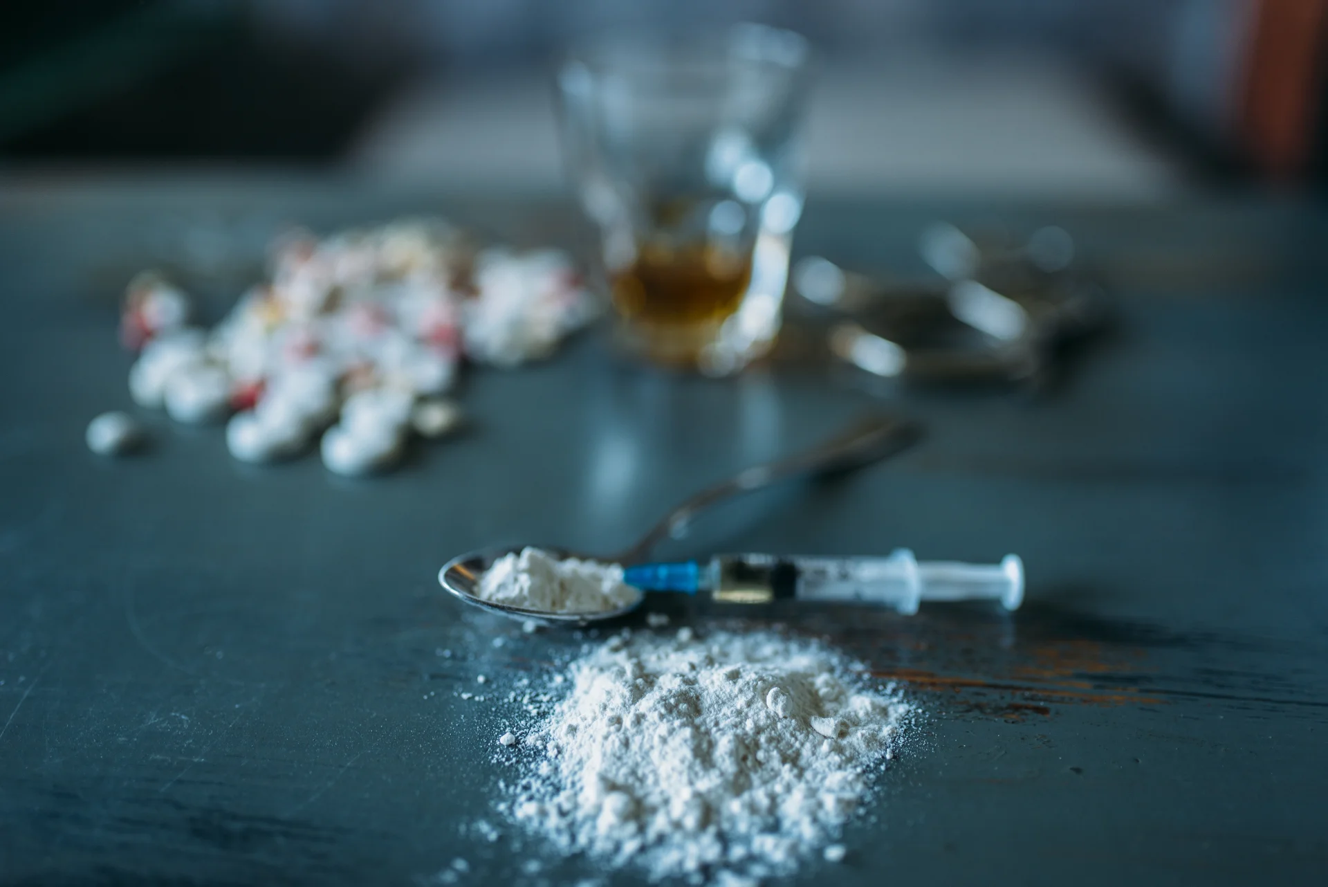 Spoon with powdered substance and syringe, representing potential misuse of ketamine, with scattered pills and a glass in the background, illustrating addiction risks associated with non-medical use.