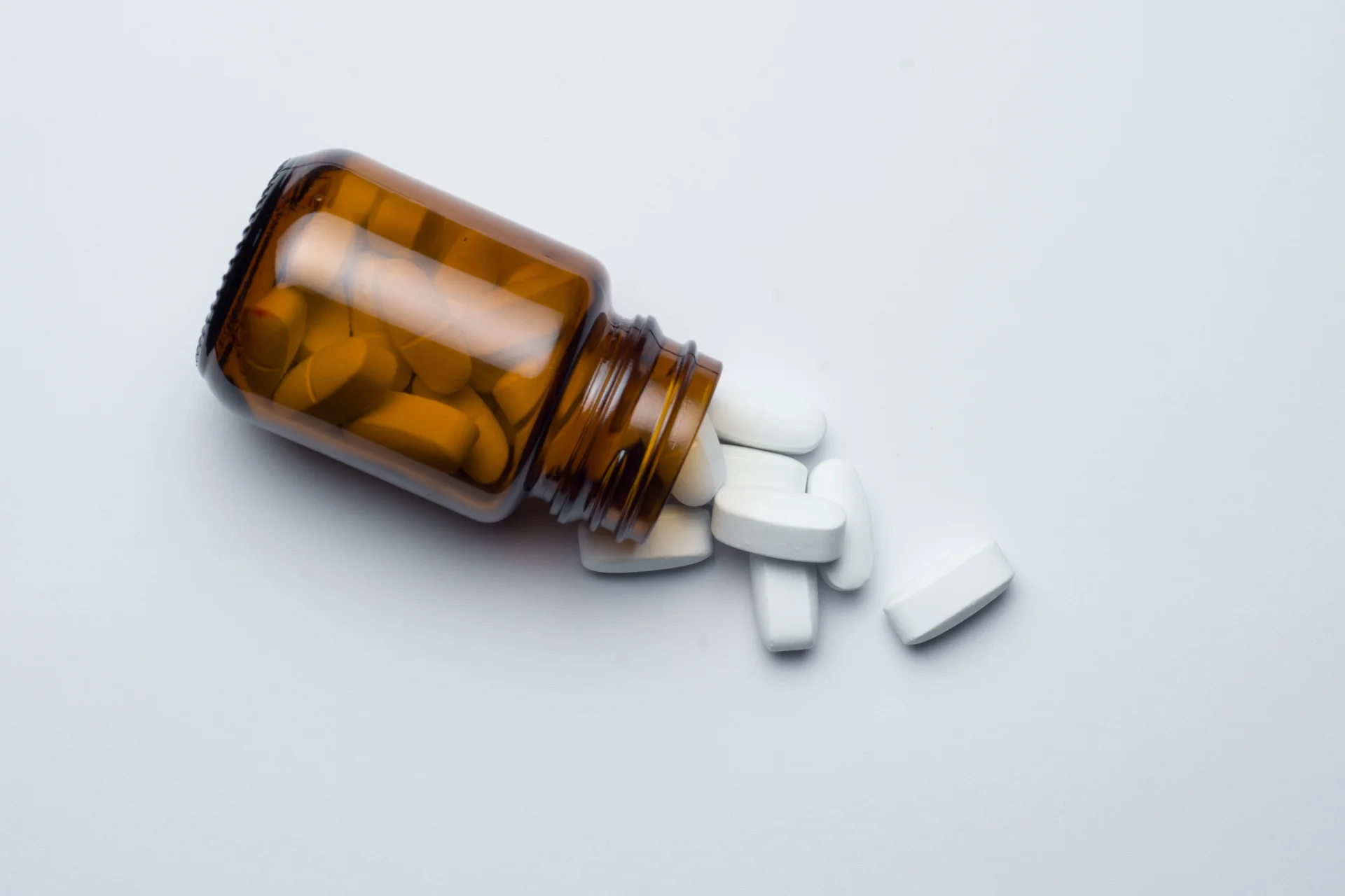 Brown prescription bottle spilling white tablets, representing Fluoxetine (Prozac) used in addiction treatment and mental health support.