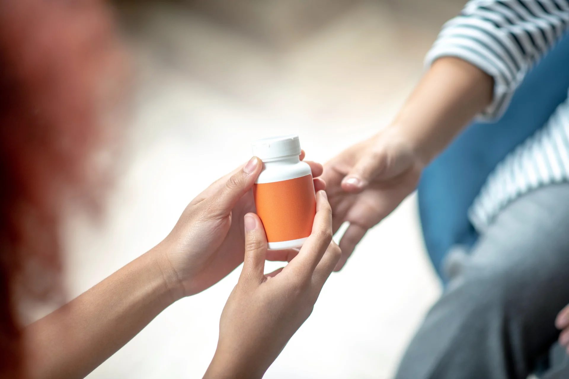 Hands exchanging a pill bottle, representing cyclobenzaprine misuse and risks associated with polysubstance use.