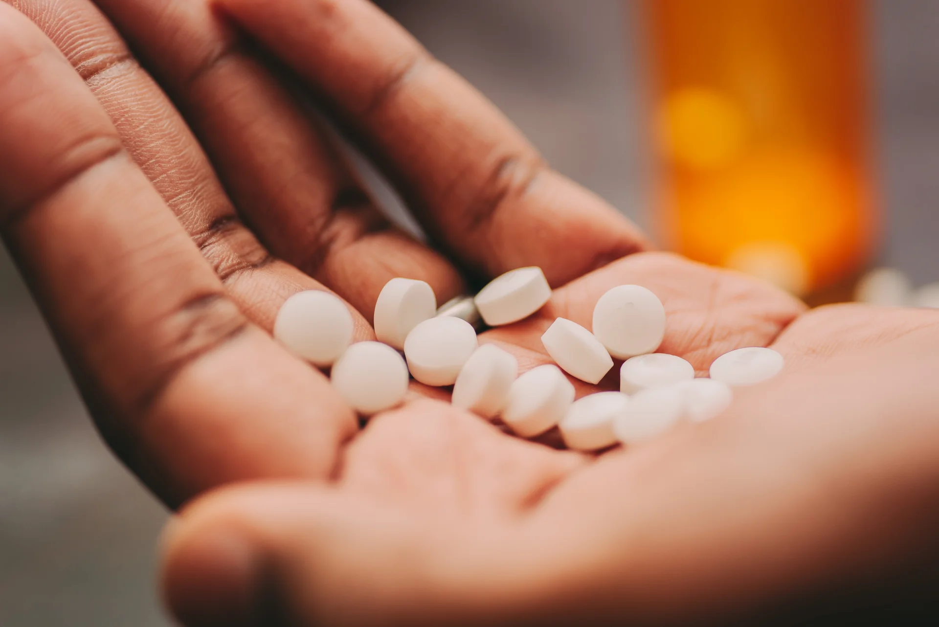 Hand holding white round pills, representing medication like Zoloft (sertraline) for mental health treatment, with a blurred prescription bottle in the background.