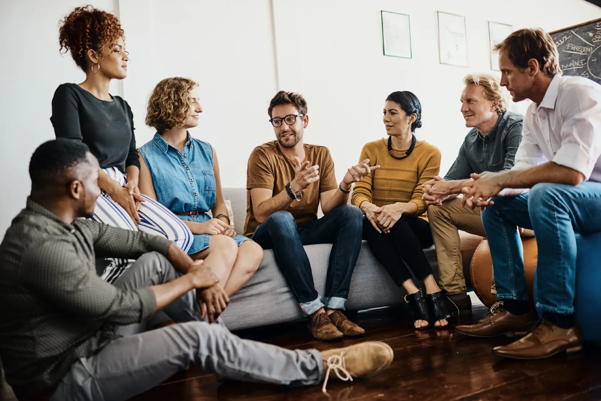 Group discussion among diverse individuals in a casual setting, focused on support and recovery concepts related to addiction and aftercare programs.