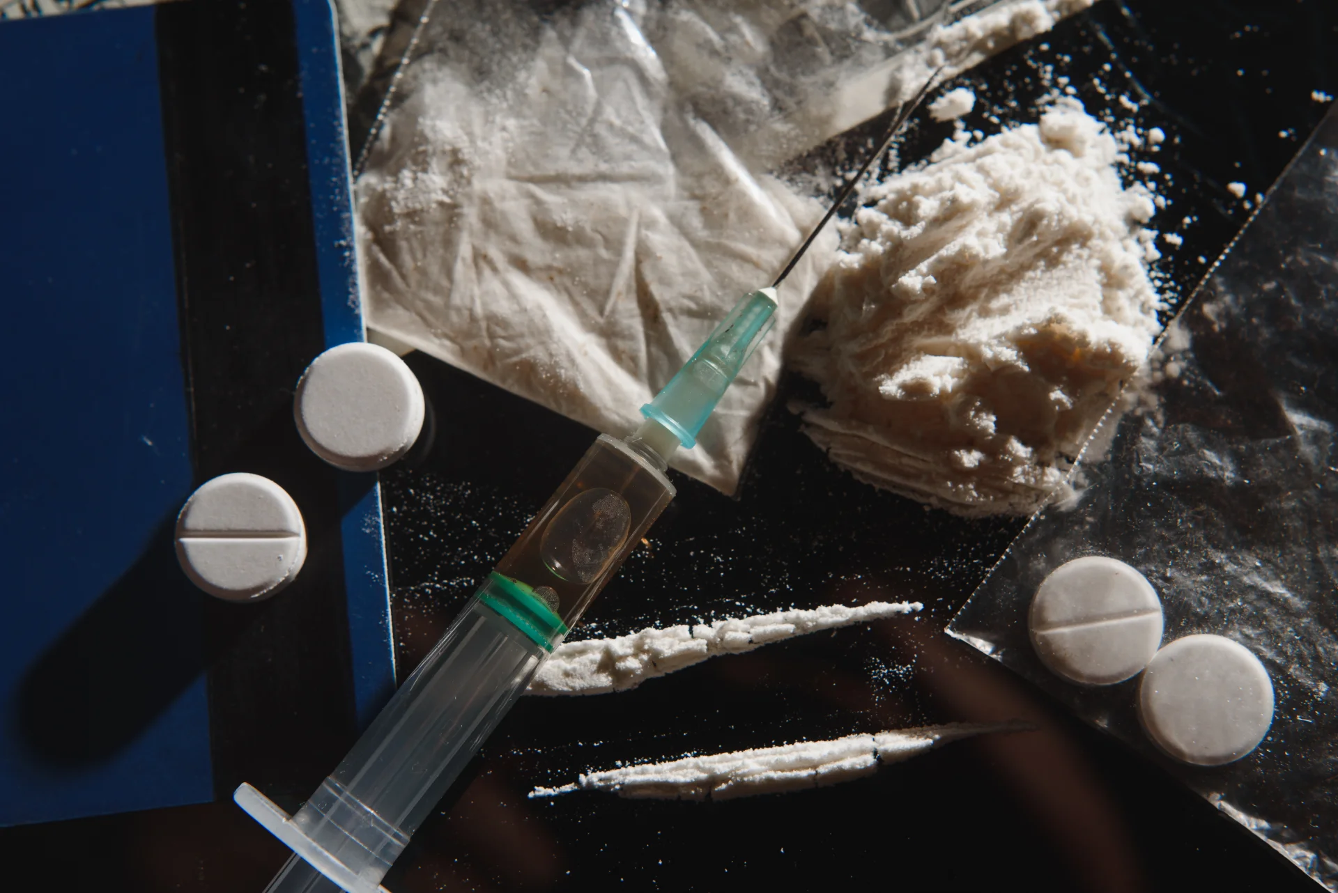 Syringe with heroin and pills on a reflective surface, illustrating the risks of opioid use and addiction.