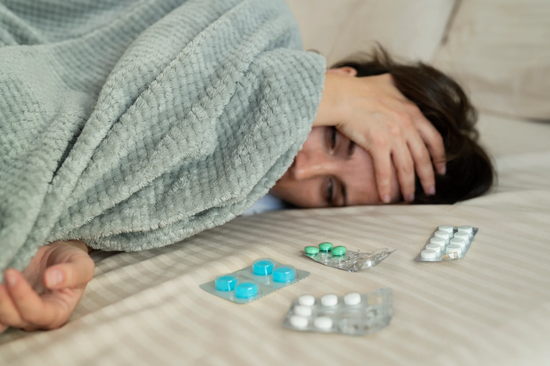 Woman lying in bed under a blanket, holding her head in distress, with various prescription pills scattered on the bed, reflecting the challenges of Valium addiction and withdrawal.